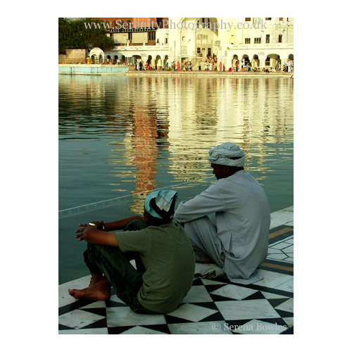 A father and son sit comtemplating life at the edge of the temple tank at the Golden Temple, Amritsar, India.